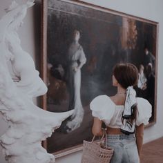 a woman standing in front of a painting and holding a wicker basket with her back to the camera