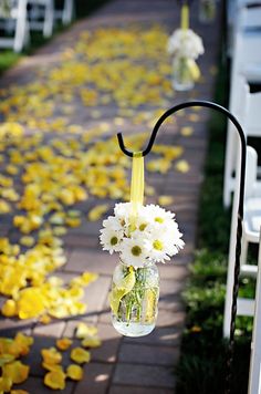 the aisle is lined with white and yellow flowers in mason jars, hanging from black metal poles