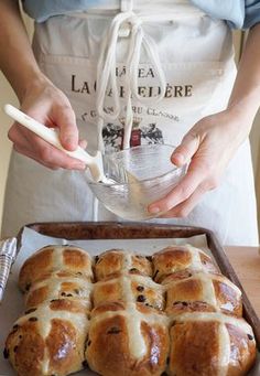 a person in an apron is making hot cross buns