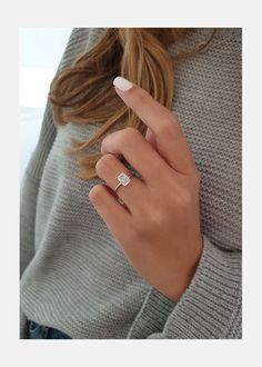 a woman's hand with a diamond ring on her left finger, wearing a gray sweater