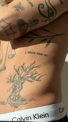 the back of a man with tattoos on his chest and arm, showing an image of a tree