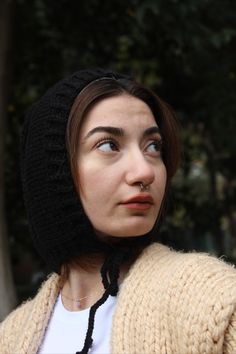 a woman wearing a black knitted hat and looking off to the side with trees in the background