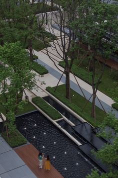 an aerial view of two people walking in the middle of a park with trees and water