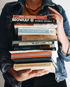 a woman holding a stack of books in her hands and wearing a jean jacket over her shoulders