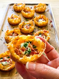 a person holding up a mini pizza in their hand with other small food items on the tray