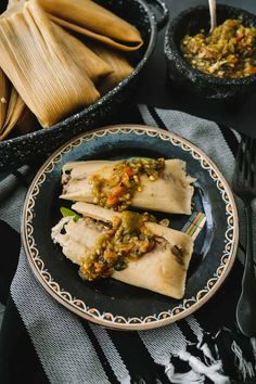 three tortillas on a black plate with green salsa and silverware in the background