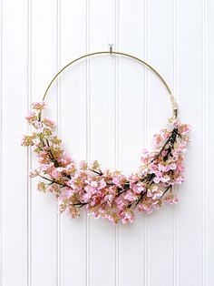 a circular wreath with pink flowers hanging from it's sides on a white wall