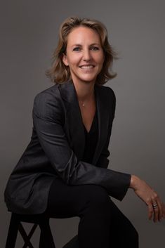 a woman sitting on top of a stool wearing a suit and smiling at the camera