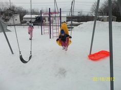 two children playing in the snow on swings and slides at a play ground with toys