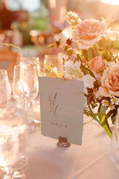 the table is set with wine glasses, flowers and place cards for guests to sit at