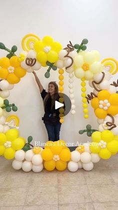 a woman standing in front of a balloon arch with yellow and white balloons hanging from it