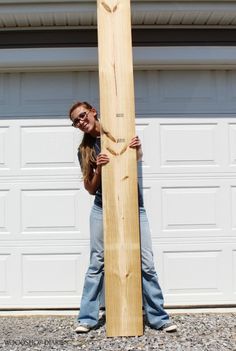 a woman standing next to a tall wooden object in front of a garage door with her hands on the top of it