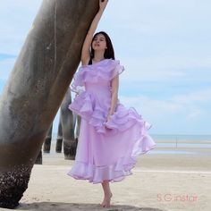 a woman in a purple dress leaning against a tree on the beach