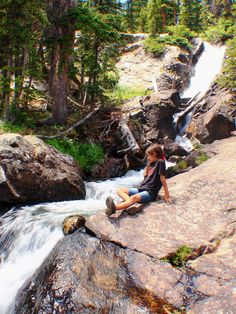 a woman sitting on top of a rock next to a waterfall