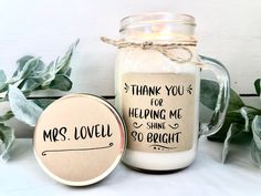 a jar filled with white candles sitting next to green leaves and a tag that says, thank you for helping me shine so bright