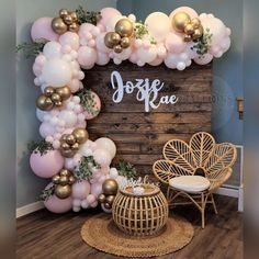 the balloon wall is decorated with gold and white balloons, greenery, and a wooden sign that says joyfae