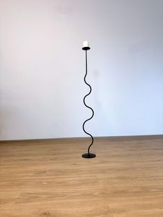 a black floor lamp with a white candle on it's end in an empty room