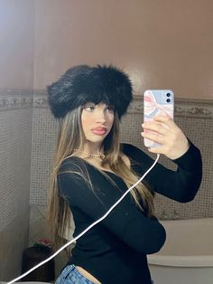 a woman taking a selfie with her cell phone wearing a furry hat and jeans