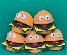 a pile of stuffed hamburgers with eyes and mouths on them sitting in front of a green wall