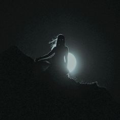 a woman sitting on top of a hill next to a bright light in the dark