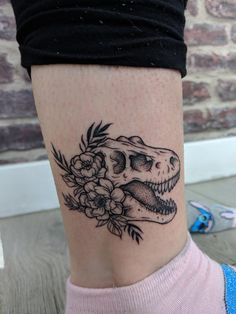 a woman's leg with a tattoo of a t - rex and flowers on it