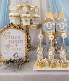 a table topped with cupcakes and cakes next to a gold plated sign