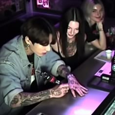 two women are sitting at a bar with tattoos on their hands and one is touching the table