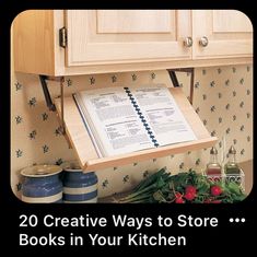 an open book sitting on top of a wooden shelf above a kitchen counter next to flowers