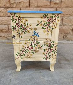 an old dresser painted with flowers and butterflies on it's sides, sitting in front of a brick wall