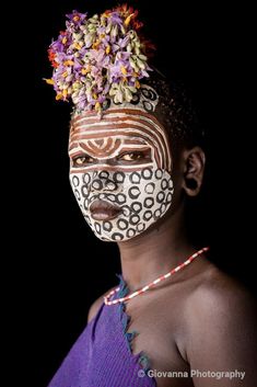 a woman with face paint and flowers on her head, in front of a black background