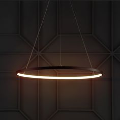 a circular light hanging from the ceiling in a dark room with geometric tiles on the wall