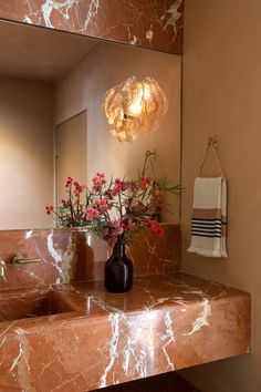 a vase with flowers sitting on a marble counter top in front of a bathroom mirror