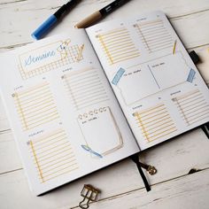 an open planner book sitting on top of a wooden table next to pens and pencils