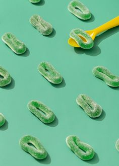 green candies are arranged on a blue surface with a yellow spoon in the middle