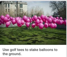 a bunch of pink balloons floating in the air on top of a grass covered field