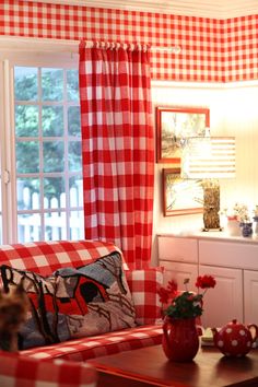 a red and white checkered couch sitting in front of a window with curtains on it