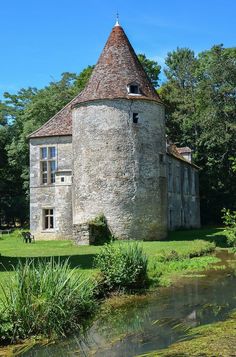 an old building with a tower next to a river in the middle of a forest