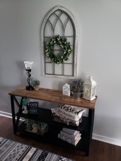 a wooden table topped with books next to a window and wreath on top of it