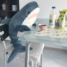 a stuffed shark sitting at a glass table with milk and cereal in front of it