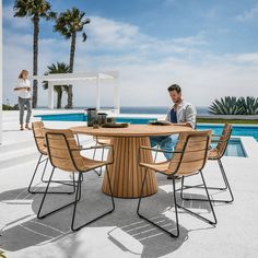 a man sitting at a table next to a pool with palm trees in the background