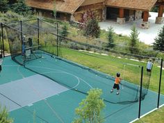 people playing tennis on an outdoor court in front of a large house with wood shingled roof