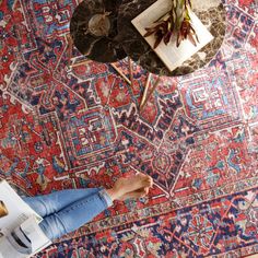 a woman sitting on top of a rug reading a book next to a coffee table