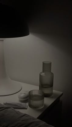 two glass vases sitting on a table next to a lamp