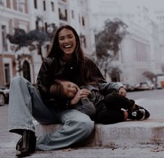 two people are sitting on the curb laughing and one is holding his head to another person's chest