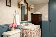 a white toilet sitting next to a sink in a bathroom under a mirror and a wooden cabinet