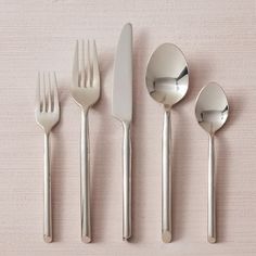 five forks, two spoons and one knife are lined up on a pink surface