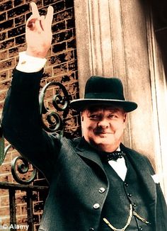 a man in a top hat and coat standing next to a gate with his hand up