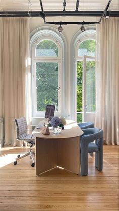 an office with two chairs and a desk in front of three large windows that look out onto the woods