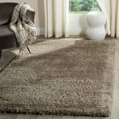 a living room area with a chair and rug on the floor, windows in the background