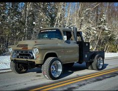 an old pickup truck is driving down the road in front of some snow covered trees